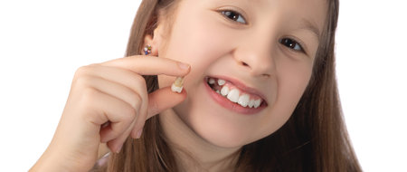 A cute little girl holds a recently removed molar in her hand and shows the place from which this...