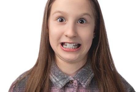 A cheerful cute girl with an orthodontic appliance makes faces on a white background. The concept of teeth alignment in childhood. Studio photo on a white background.の写真素材