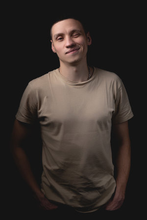 Handsome young man posing over black background. Studio photo with one light source. Smiling guy cheerfully posing in the studio.の写真素材