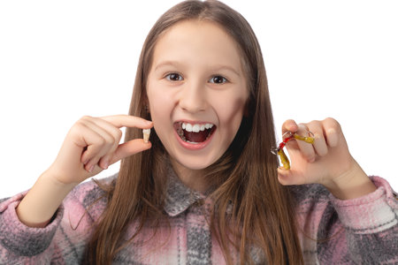 A cute little girl is holding her molar tooth in one hand and holding a colorful orthodontic appliance in the other hand. Studio photo isolated on white background.の写真素材