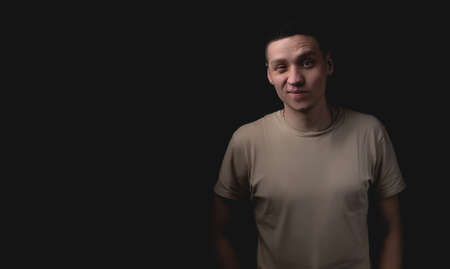 Handsome young man posing over black background. Studio photo with one light source. The guy puts his hands in his pockets and expresses doubt.の写真素材