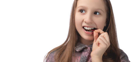 A cute little girl is putting on an orthodontic appliance. The concept of oral hygiene in childhood. Studio photo on a white background.の写真素材