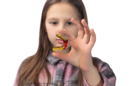 Cute little girl posing in the studio holding an orthodontic appliance in her hand. The concept of oral hygiene in childhood. Photo on a white background.の写真素材