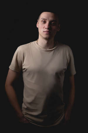 Handsome young man posing over black background. Studio photo with one light source. Smiling guy cheerfully posing in the studio. The serious guy looks in front of him good-naturedly.の写真素材
