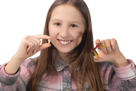 A cute little girl is holding her molar tooth in one hand and holding a colorful orthodontic appliance in the other hand. Studio photo isolated on white background.の写真素材