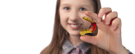 Cute little girl posing in the studio holding an orthodontic appliance in her hand. The concept of oral hygiene in childhood. Photo on a white background.の写真素材
