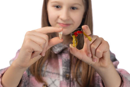 A cute little girl is holding her molar tooth in one hand and holding a colorful orthodontic appliance in the other hand. Studio photo isolated on white background.の写真素材