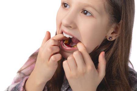 A cute little girl is putting on an orthodontic appliance. The concept of oral hygiene in childhood. Studio photo on a white background.の写真素材