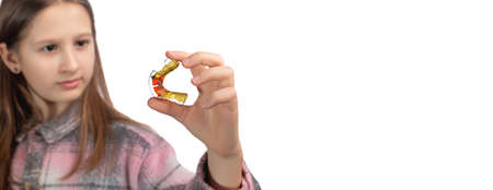 Cute little girl posing in the studio holding an orthodontic appliance in her hand. The concept of oral hygiene in childhood. Photo on a white background.の写真素材