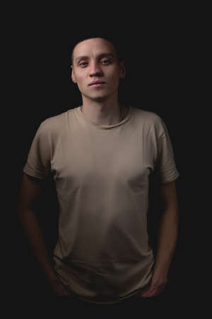 Handsome young man posing over black background. Studio photo with one light source. The guy looks in front of him approvingly with his hands in his pockets.の写真素材