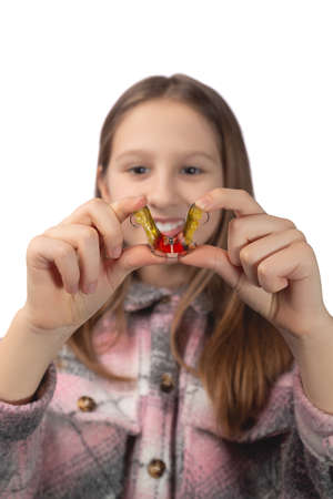 Cute little girl posing in the studio holding an orthodontic appliance in her hand. The concept of oral hygiene in childhood. Photo on a white background.の写真素材