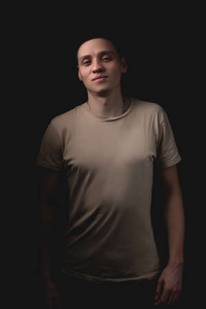 Handsome young man posing over black background. Studio photo with one light source. Smiling guy cheerfully posing in the studio.の写真素材