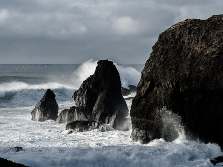 Waves crash against rugged volcanic cliffs at ValahnÃºkamÃ¶l, sending sea spray into the air....
