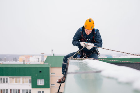 Industrial climber in uniform and helmet sitting on the roof preparing to the work in winter