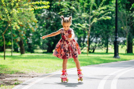 Little pretty girl on roller skates in dress in park. Cheerful child having fun outdoorsの写真素材