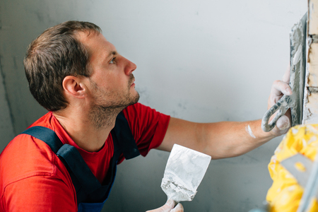 Man in red shirt and blue overall with putty knife doing puttyの写真素材