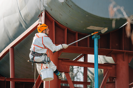 Industrial climber in helmet and uniform painting water tower. Professional Painter working on height. Risky job. Extreme occupation.の写真素材
