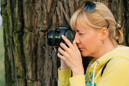 Girl with professional camera in hands. Close up of female photographer in park.の写真素材