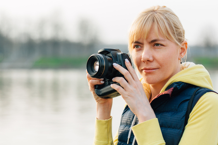 Girl with professional camera in hands. Close up of female photographer in park.の写真素材