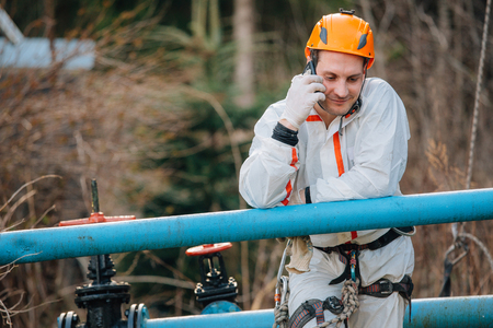 Industrial climber having a phone call with his smartphone. Professional workman using phoneの写真素材