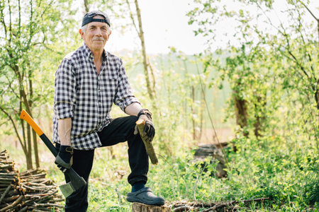 Senior man in baseball cap with axe chopping wood. Elderly arborist man working in garden. Active retirement lifestyle concept.の写真素材