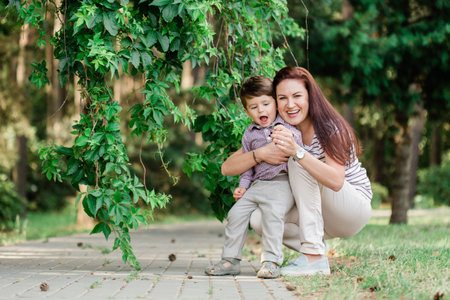 Happy mother with cute little boy having fun outdoors. Cheerful woman playing with her son in park....