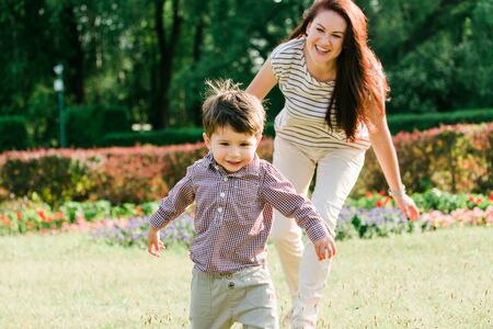 Mother having fun with cute son in summer park. Happy woman with cheerful little boy outdoorsの写真素材