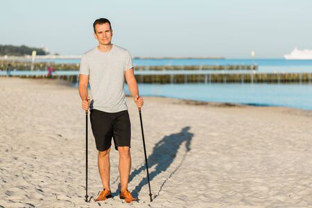 Pretty young man resting after nordic walking on the beach. Healthy sport life conceptの写真素材