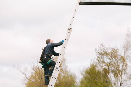 Industrial climber going up the ladder to the billboard. Risky job. Work on heightの写真素材