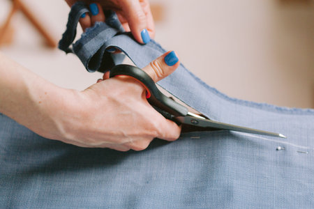 Close up. Tailor cutting a roll of fabric on which she has marked out the pattern of the garment she is making with tailors chalk.の写真素材
