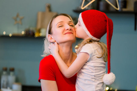 Mother with Happy cheerful Little girl in santa hat sitting at the festive table. Christmas time. Woman having fun with daughterの写真素材