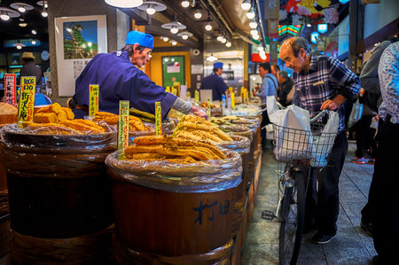 Nishiki Market, Kyoto, Japan  â October 22, 2016 : Old man came with his bicycle stood in front of a store which sells variety of pickled food. He is asking for one of them to the vendor.のeditorial素材