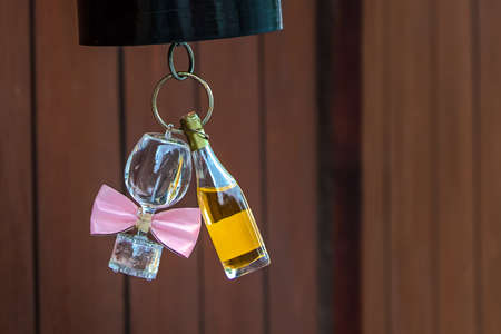 Still life - bottle of wine and wine glass. A bottle of wine, and a wine glass with pink bow tie attached are hung to the bottom of red paper lampshade.の写真素材