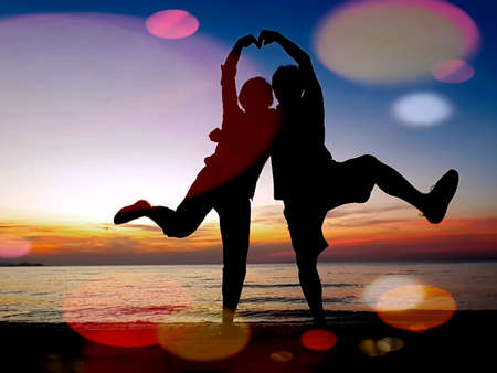 COUPLE IN LOVE. A couple on a beach poses with their arms cupped together forming heart shape.の写真素材