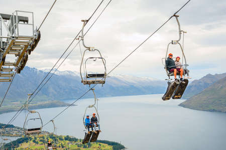 Queenstown, NZ â April 15, 2018: Fun riders on a steep cable chair lift carrying them and their carts up to the top of hill slope for a luge ride with beautiful views of Lake Wakatipu and Queenstown.のeditorial素材