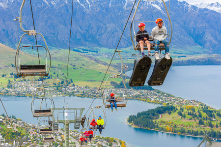 Queenstown, NZ â€“ April 15, 2018: Fun riders on a steep cable chair lift carrying them and...