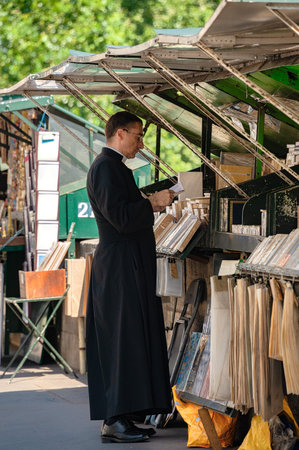 Paris, France - July 04, 2017 : A priest in cassock garment glances at a book from one of the book stalls along River Seine sidewalk. These book stalls are one of the most iconic symbols of Paris.のeditorial素材