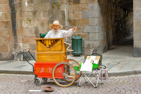 Saint-Malo, France - July 20, 2017: An old man with long white bread stands behind his street organ chanting and singing while playing his musical instrument for tips.のeditorial素材