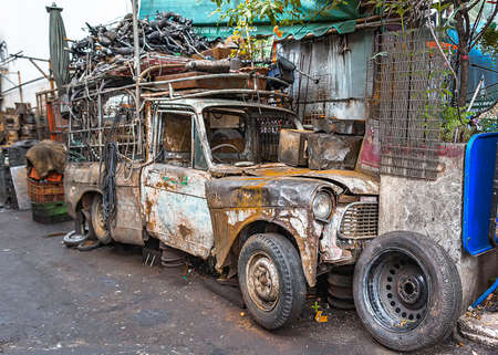 Wrecked pickup truck with pieces of used spare parts on its top, left abandoned along alleyway.のeditorial素材