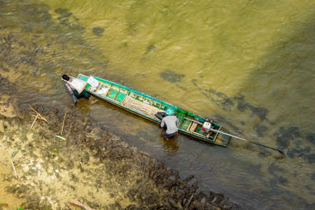 Kanchanaburi, Thailand - September 6, 2020: View from above, a villager having sacksful of goods strapped to her forehead as she leaves the long tail boat while the drive keeps the boat still.のeditorial素材