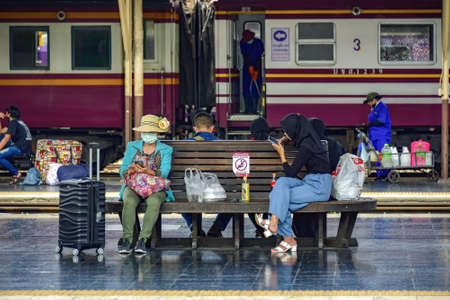 Bangkok Train Station - Hau Lumphong, Thailand - March 20, 2021: Commuters sit on a platform bench waiting for their train to arrive Everyone wears a facemask and keeps their social distance.のeditorial素材