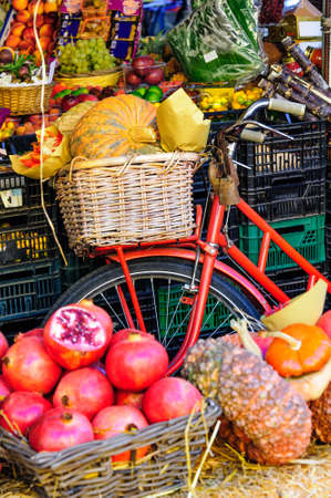 A classic fruit and vegetable display at a market stall using a vintage bicycle with a basket carrying a big pumpkin.の写真素材