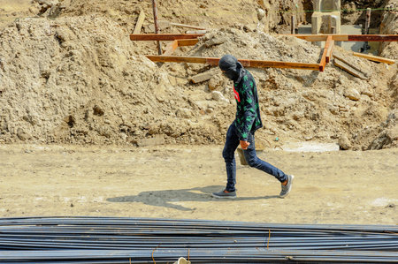A construction worker on site carrying a bucketful of sand walks hastily in the scorching sun.の写真素材