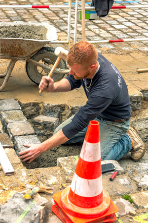 Dinan, France â April 12, 2022: Cobblestone Street. A worker is a re-paving quarried stone on the driveway.のeditorial素材