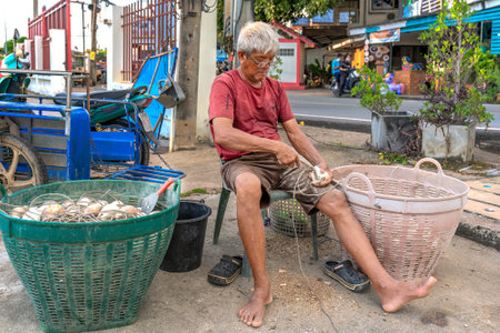 Chonburi, Thailand, Nov. 28, 2022: A fisherman scraps barnacles off seashells. They are used as bait for catching octopuses.のeditorial素材