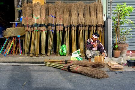 Bangkok, Thailand, May 30, 2022: A worker works on a footpath in front of a store selling coconut stalk brooms and other tools.のeditorial素材