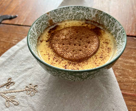 custard cream with biscuit and cinnamon in a bowl on wooden tableの写真素材