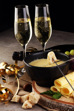 Gourmet Swiss fondue dinner on a winter evening with assorted cheeses on a board alongside a heated pot of cheese fondue with two forks dipping bread and white wine behind in a tavern or restaurantの写真素材