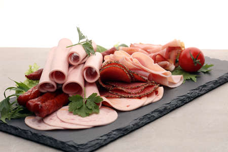 Food tray with delicious salami, pieces of sliced ham, sausage, tomatoes, salad and vegetable - Meat platter with selectionの写真素材