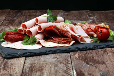 Food tray with delicious salami, pieces of sliced ham, sausage, tomatoes, salad and vegetable - Meat platter with selectionの写真素材